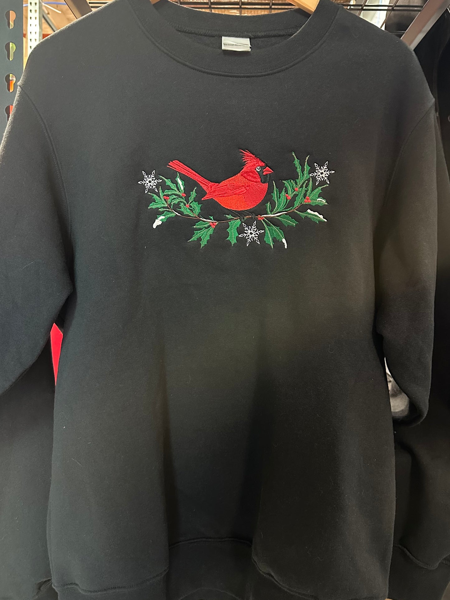 Black sweatshirt with a red cardinal and greenery design on a hanger.